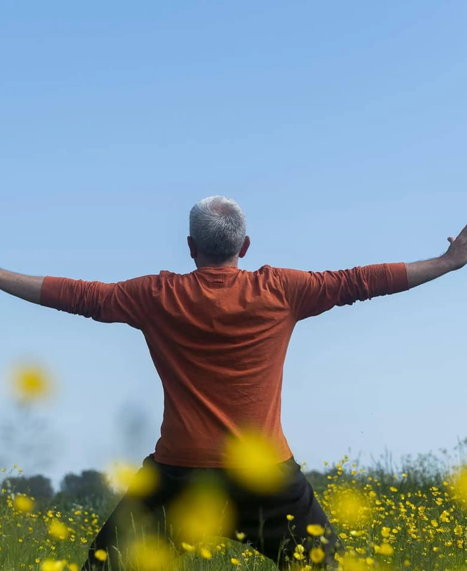 A practitioner outdoors with arms wide open in a field of flowers