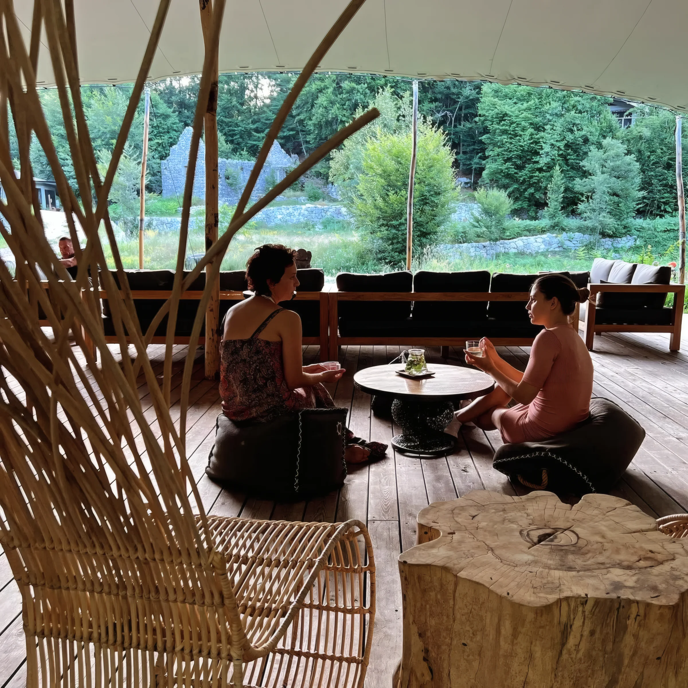 Two people practising together in the open pavilion at ašuma retreat, with the forest behind