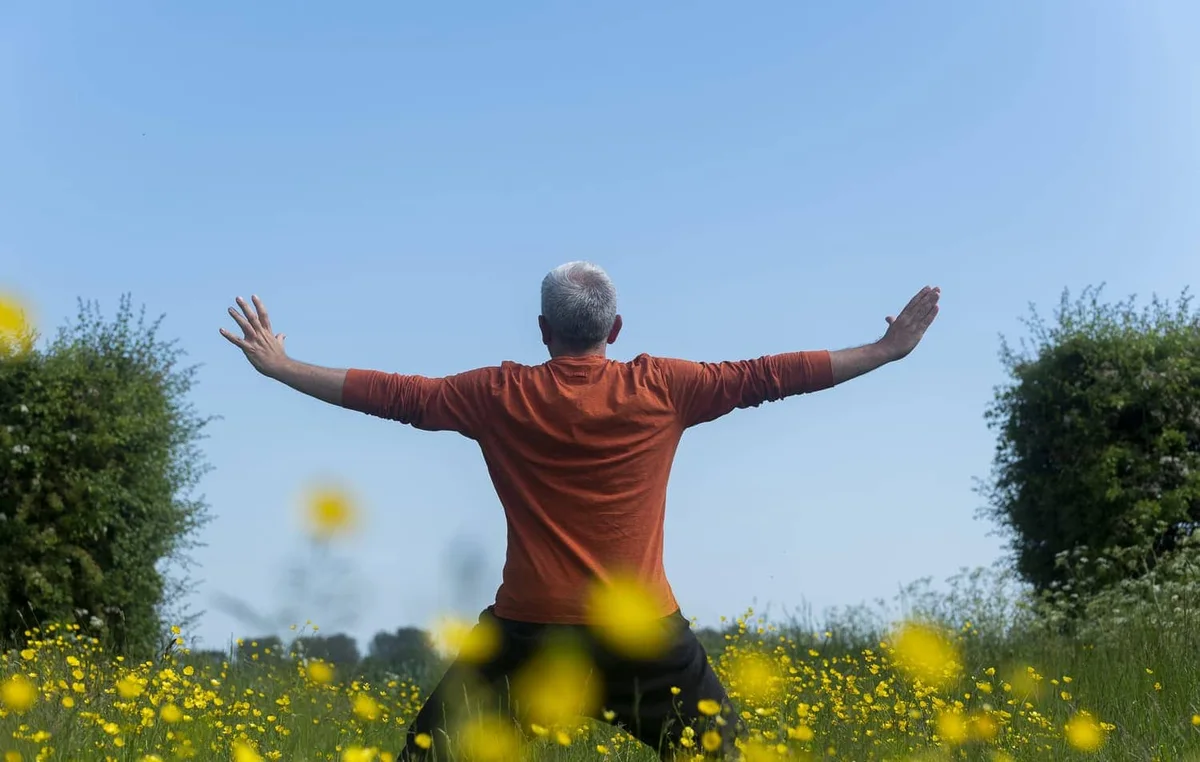 John Millar from behind, arms open towards a wide summer meadow