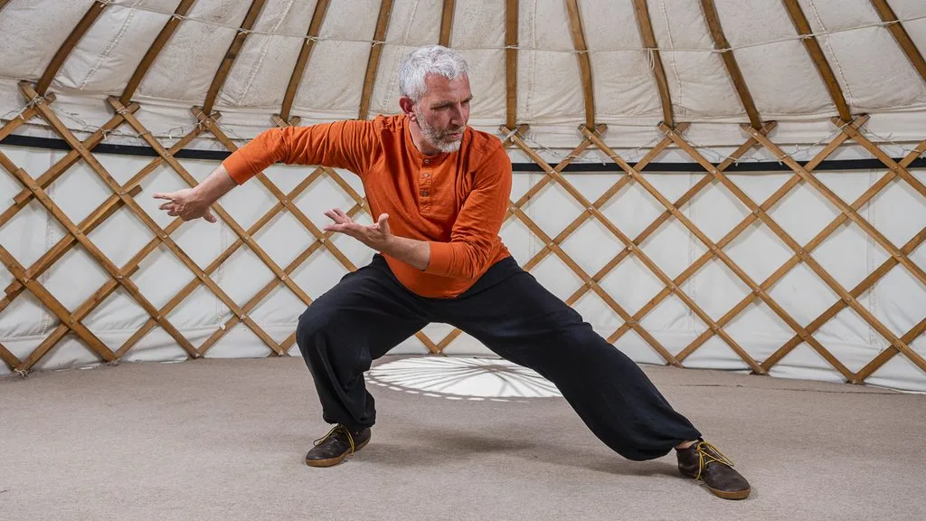 John Millar in a wide stance in the yurt, arms flowing to one side