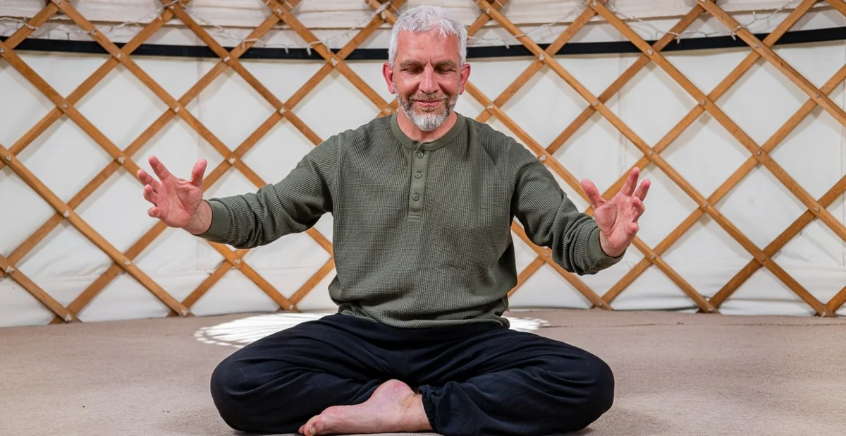 John Millar sitting cross-legged in the yurt, hands open and relaxed